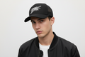Person wearing a black cap with a logo and text, against a plain background