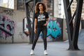 Person wearing a black t-shirt with text, standing in an urban setting with graffiti.